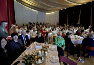 Na zdjęciu widać siedzących przy świątecznie przystrojonych stolikach rodziców, nauczycieli i zaproszonych na koncert gości.