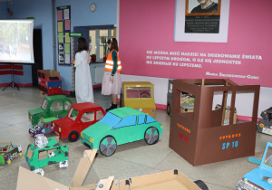 Na zdjęciu, na tle obrazu z patronką szkoły, konstrukcje kartonowych samochodów wykonanych przez uczniów naszej szkoły.