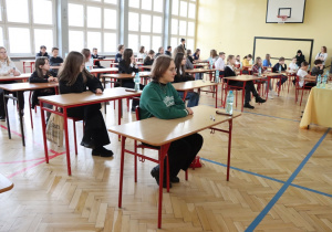 Na zdjęciu widać uczestników konkursu siedzących w ławkach na sali gimnastycznej.