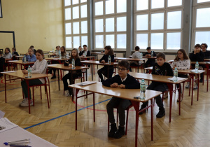 Na zdjęciu widać siedzących w sali gimnastycznej uczestników konkursu.