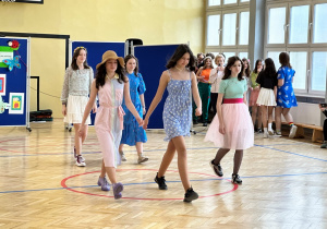 Uczniowie w sali gimnastycznej prezentują wiosenną kolekcję mody.