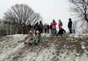 Na zdjęciu uczniowie podczas zajęć wychowanie fizycznego zjeżdżają z ośnieżonej górki.