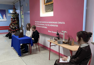 Na zdjęciu widać uczestników uroczystej akademii. W tle choinka i portret Marii Skłodowskiej - Curie.