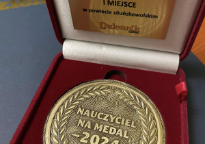 Na zdjęciu pamiątkowy medal z napisem "Nauczyciel Na Medal" dla Pani Anny Kowalczyk za zajęcie pierwszego miejsca w kategorii "Nauczyciel klas I - VIII" w powiecie zduńskowolskim.