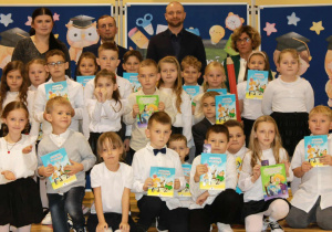 Na zdjęciu stoją uczniowie klasy 1a z wychowawcą, dyrekcją i zaproszonymi gośćmi.