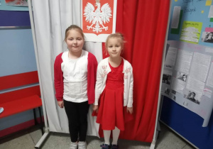 Uczniowie z klasy 1a stoją na tle flagi biało - czerwonej i godła narodowego.