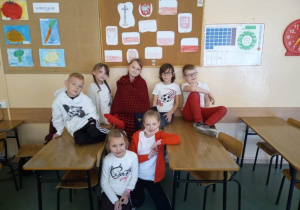 Uczniowie z klasy 1a siedzą w pracowni na ławkach ubrani w stroje biało - czerwone.