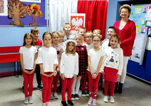 Na zdjęciu stoją, na tle flagi biało - czerwonej i godła, uczniowie z klasy 1a ze swoją wychowawczynią Panią Beatą Łasochą.