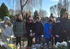 Uczniowie stoją na cmentarzu przy grobach zmarłych pracowników SP 10.