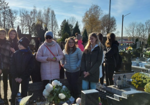 Uczniowie stoją na cmentarzu przy grobach zmarłych pracowników SP 10.