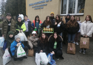 Na zdjęciu widać uczniów kl. 7a stojących przed budynkiem szkolnym z darami dla Ukrainy.