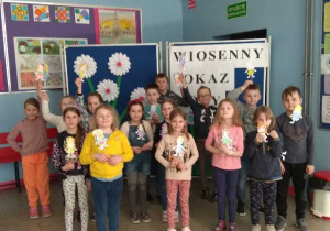 Na zdjęciu widać uczniów klasy Ia, stojących na tle wiosennej gazetki. Dzieci trzymają wykonane przez siebie wizerunki Marzanny.