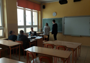 Na zdjęciu widać siedzących w klasie uczniów, dwoje spośród nich zajęło miejsce nauczyciela i prowadzą zajęcia.
