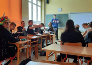Na zdjęciu widać siedzących w klasie uczniów, jeden z nich zajął miejsce nauczyciela i prowadzi zajęcia.