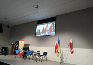 Zdjęcie przedstawia ekran projekcyjny, na którym widoczna jest wideokonferencja.