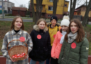 Na zdjęciu widać stojących na dworze uczestników konkursu. Jedna z uczennic trzyma koszyczek z czerwonymi jajakami.