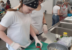 Uczestnicy konkursu podczas przygotowywnia potraw. Uczennice pracują przy kuchennym stole.