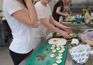 Uczestnicy konkursu podczas przygotowywnia potraw. Uczennice pracują przy kuchennym stole.
