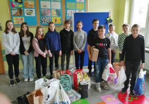 Na zdjęciu widać stojących na korytarzu uczniów - członków Szkolnego Klubu Wolontariatu z zebranymi darami dla dziaci z Ukrainy.