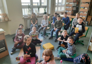 Dzieci z klas pierwszych siedzą na podłodze w szkolnej bibliotece.