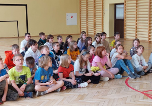 Na zdjęciu widać siedzących uczniów na sali gimnastycznej.